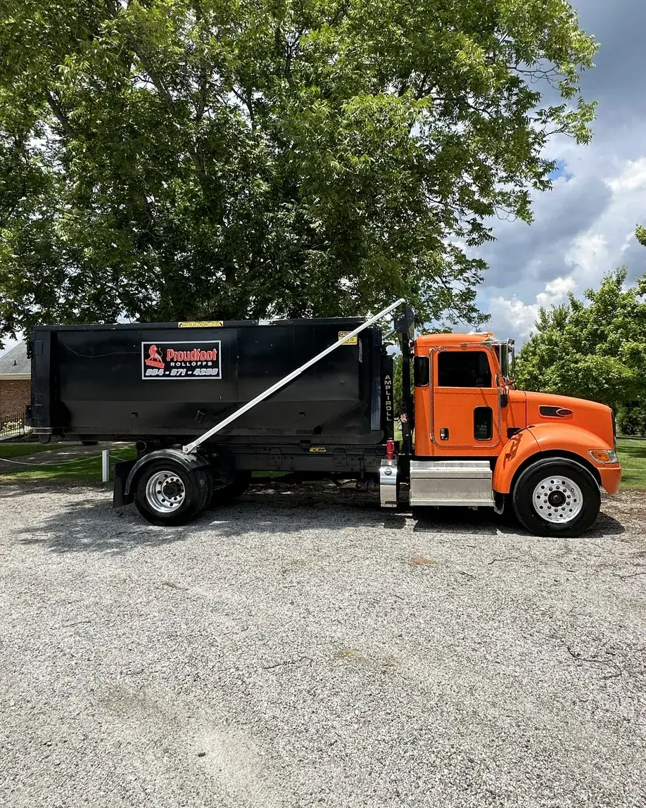 A Proudfoot Rolloffs roll-off truck with a loaded dumpster on the gravel at the Donalds yard