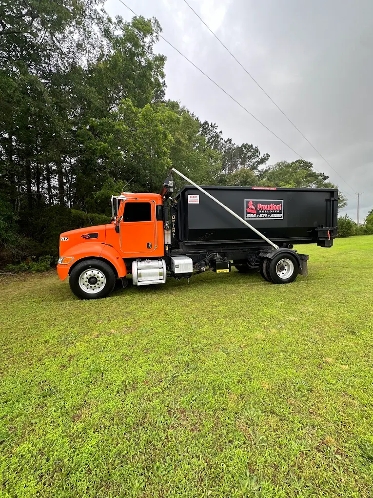 Proudfoot Rolloffs truck delivering a black roll-off dumpster to a yard